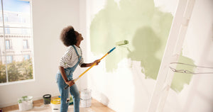Junge Frau streicht Wand mit freude und grüner Naturfarbe. Fotografiert von "VAKSMANV".